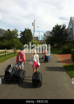 Padre con due bambini che camminano giù per strada tirando valigie, Norvegia Foto Stock