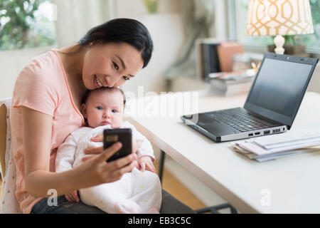 Asian la madre e il bambino tenendo selfie in home office Foto Stock