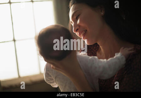 Asian madre holding baby vicino a finestra Foto Stock