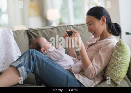 Asian madre assunzione cellulare fotografia del bambino nella stanza vivente Foto Stock