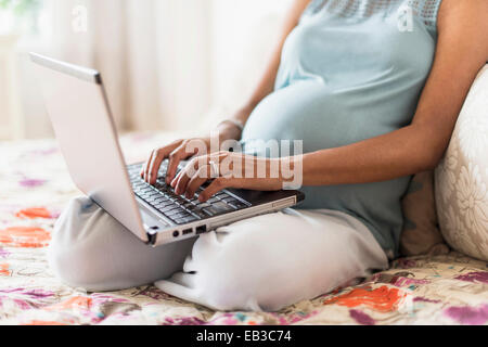 Africana incinta madre americana utilizzando computer portatile a letto Foto Stock
