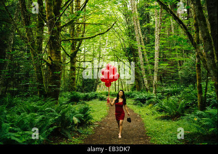 Donna coreana holding palloncini rossi nella lussureggiante foresta Foto Stock