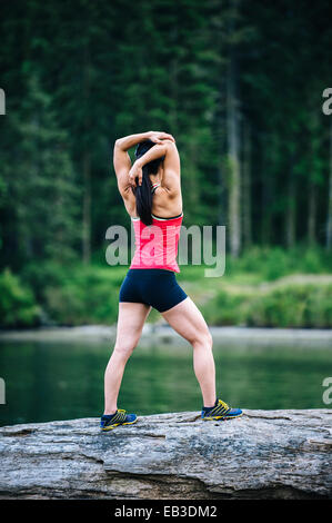 Il coreano runner stiramento sulla roccia vicino al lago Foto Stock