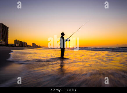 Vista offuscata di silhouette dell uomo la pesca in onde sulla spiaggia al tramonto Foto Stock