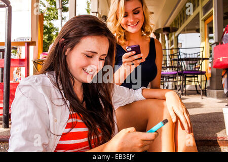 Caucasian ragazze adolescenti utilizzando i telefoni cellulari in città Foto Stock