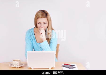 Stanco o annoiato giovane donna seduta a home office desk nella parte anteriore del computer portatile sbadigli Foto Stock