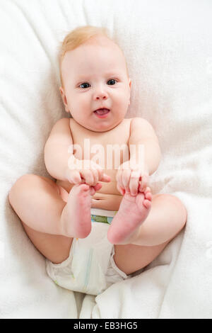 Bambino giacente sul letto e tenendo le gambe Foto Stock