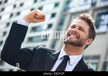 Un giovane uomo di successo, maschio imprenditore esecutivo a braccia alzate per celebrare il tifo urlando di fronte ad un alto blocco di office Foto Stock