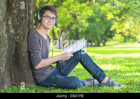 Giovane studente in park ascoltare musica sulle cuffie Foto Stock