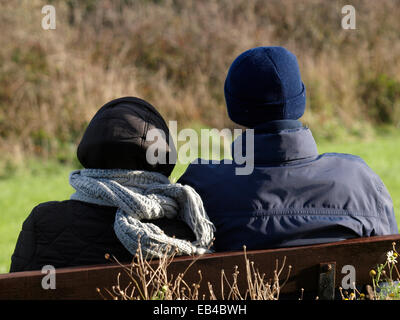 Adulto Giovane seduto su una panchina pubblica in inverno, Padstow, Cornwall, Regno Unito Foto Stock