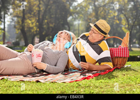 Coppia matura ascoltando musica sulle cuffie in park in una giornata di sole Foto Stock