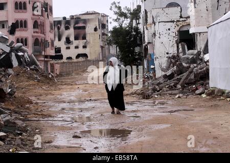 La città di Gaza, Striscia di Gaza, Territori palestinesi. 26 Nov, 2014. Una donna Palestinese passeggiate passato le rovine di una casa che è stata distrutta durante il periodo di sette settimane offensiva israeliana sulla Striscia di Gaza, come l'operazione di rimuovere resti iniziato nel quartiere Shijaeya, a est di Gaza City, 26 novembre 2014. Dopo la guerra di Gaza si è conclusa il 26 agosto 2014 Israele ha permesso una piccola quantità di materiale da costruzione nella Striscia di Gaza per aiutare la ricostruzione di alcune decine di migliaia di case distrutte dagli attacchi aerei e di artiglieria, ma non è palpabilmente alleviato il blocco © Mohammed Asad/immagini APA/ZUMA filo/Alamy Live News Foto Stock