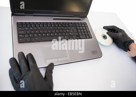 Ladro hacking e mettendo un cd-rom nel computer portatile Foto Stock