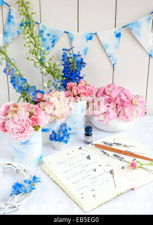 Notebook con note sull'estate, penna, inchiostro, lavanda, delphinium, rosa rose, garofani, ortensie, bunting, su sfondo bianco Foto Stock