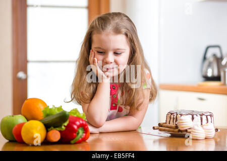 Bambino scegliendo tra ortaggi sani e gustosi dolci Foto Stock