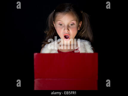 Una graziosa bambina apre il suo regalo di Natale su sfondo nero Foto Stock