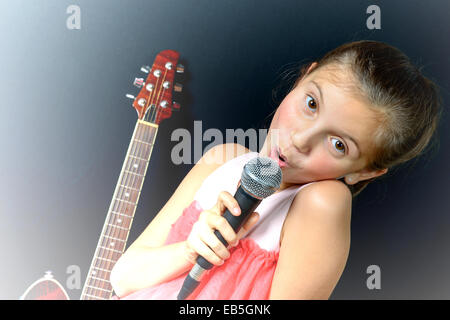 Una giovane ragazza a cantare con un microfono e chitarra Foto Stock