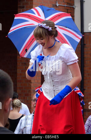 Donna in costume Costume su palafitte tenendo un Unione Jack ombrello, Stourbridge Carnvial, West Midlands, England, Regno Unito Foto Stock