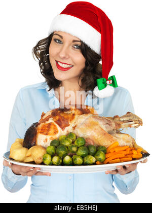 Giovane donna in rosso Santa Hat tenendo il tacchino arrosto e verdura pronta da mangiare per il pranzo di Natale isolata contro uno sfondo bianco Foto Stock