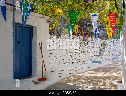 Kioni, Itaca, Isole Ionie, Grecia. Colorati stemmi religiosi appeso sopra pitturato di bianco tipico vicolo del villaggio. Foto Stock
