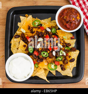 Il peperoncino e formaggio Cheddar Nacho piatto con pomodori freschi, cipolle, peperoni Jalapeño, panna acida e salsa Foto Stock