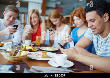 Gli amici seduti al Café assorbito nei loro telefoni Foto Stock