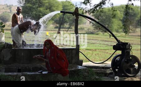 Due uomini li lavaggio auto a una pompa per acqua e una donna lavando le mani in India Foto Stock