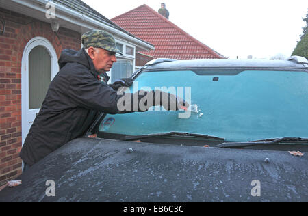 Un uomo anziano frost di raschiatura di un parabrezza di automobile su un gelido mattino. Foto Stock