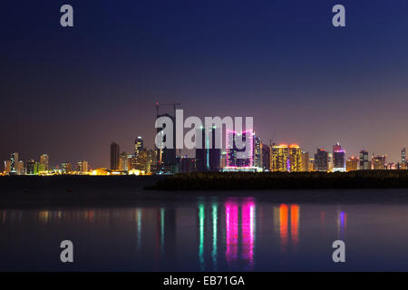 Notte moderno skyline della città con brillanti luci e riflessi nell'acqua. Manama, la capitale del Bahrein, Medio Oriente Foto Stock
