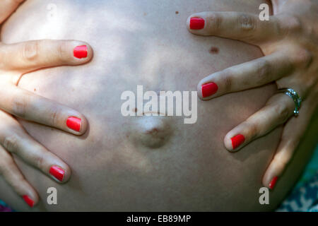 Pancia donna incinta, unghie dipinte di rosso, pancia incinta enorme Foto Stock