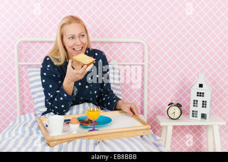 Donna di mezza età è avere la colazione a letto Foto Stock