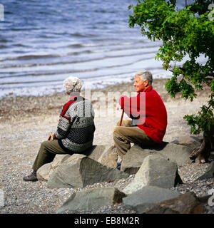 Uomo maturo e la moglie seduta sulle rocce accanto al lago Foto Stock