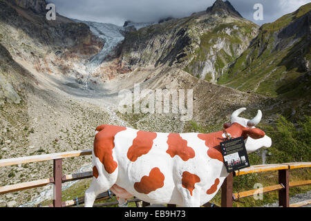 Un modello di vacca da latte di fronte al rapido calo Glacier de pre de bar di Mont Blanc range, Italia. Appropriate come le emissioni di metano provenienti dalle vacche sono un driver del cambiamento climatico. Foto Stock