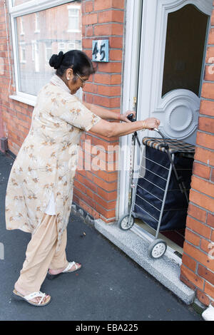 Donna anziana la manovra del carrello attraverso la porta della sua casa, Foto Stock