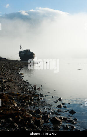 Distrutto la barca si trova sulle rive di Loch linnie come brume con il Ben Nevis in background Foto Stock