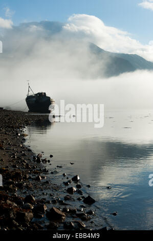 Distrutto la barca si trova sulle rive di Loch linnie come brume con il Ben Nevis in background Foto Stock