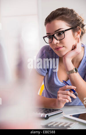 Giovane donna che indossa il corno-bordati di occhiali, lavorando in ufficio sul PC desktop, Germania Foto Stock