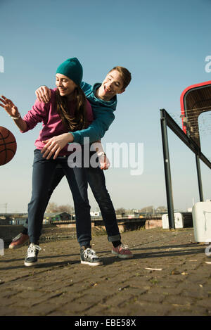 Ragazzo adolescente e una ragazza giocare a basket all'aperto, area industriale, Mannheilm, Germania Foto Stock