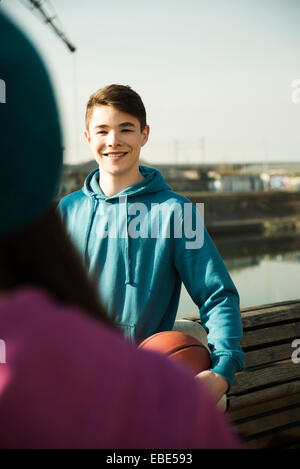 Ragazzo Teeange holding basket all'aperto, sorridente e guardando la teenager, area industrail, Mannheim, Germania Foto Stock