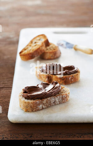 Fette di Baguette e rabboccato con Noccioletta sulla lastra di marmo su sfondo di legno, Studio Shot Foto Stock