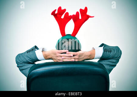 Un uomo con una renna palchi con archetto rilassante nella sua sedia per ufficio dopo un ufficio Christmas party Foto Stock