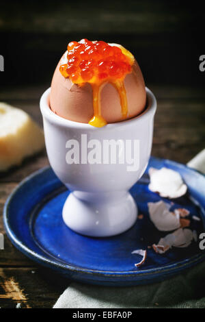 La prima colazione con soft-uova sode con caviale rosso in bianco eggcup, servita con pane su un vecchio tavolo di legno. Vedere serie Foto Stock