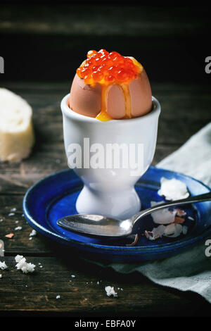 La prima colazione con soft-uova sode con caviale rosso in bianco eggcup, servita con pane su un vecchio tavolo di legno. Vedere serie Foto Stock