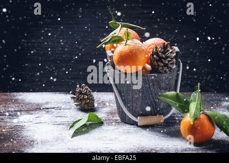 Cucchiaio di legno con i tangerini su sfondo di legno con la neve e il cono. Foto Stock