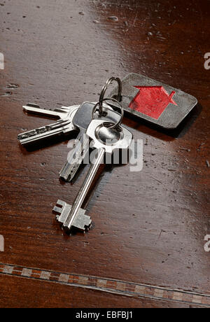 Set di chiavi di casa con un rosso portachiavi su legno marrone scuro tabella Foto Stock