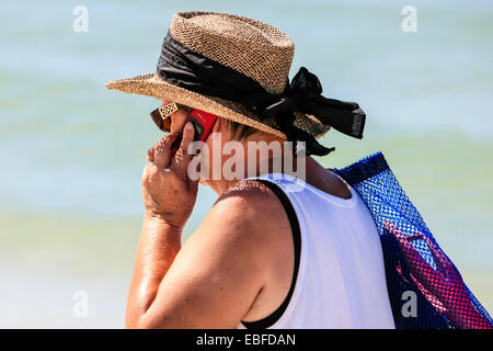 Attiva una femmina senior in profonda conversazione sul suo cellulare come lei cammina lungo la spiaggia di Sarasota FL Foto Stock