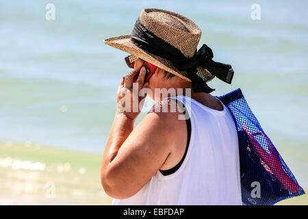 Attiva una femmina senior in profonda conversazione sul suo cellulare come lei cammina lungo la spiaggia di Sarasota FL Foto Stock