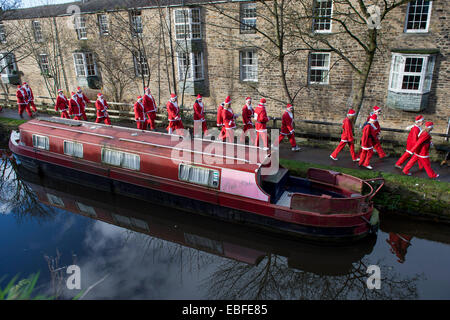 Persone (uomini, donne e bambini) vestita in rosso e bianco di Babbo Natale abiti sono passeggiate, jogging, in esecuzione passato canal barche & prendendo parte alla grande Skipton Santa Fun Run, una raccolta di fondi annuale gara di beneficenza organizzata dal Rotary Club - Molle Ramo di Leeds Liverpool Canal alzaia, Skipton Town Center, North Yorkshire, Inghilterra, Regno Unito. Foto Stock