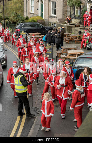 Persone (uomini, donne e bambini) vestita in rosso e bianco di Babbo Natale abiti sono passeggiate, jogging, esecuzione e prendendo parte alla grande Skipton Santa Fun Run, una raccolta di fondi annuale gara di beneficenza organizzata dal Rotary Club - Skipton Town Center, North Yorkshire, Inghilterra, Regno Unito. Foto Stock