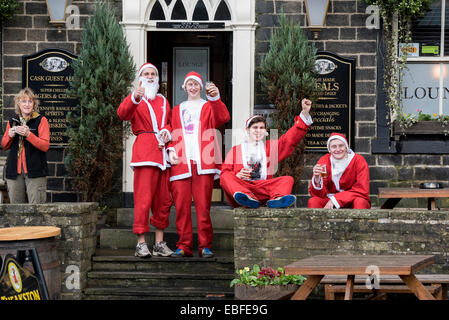 Al di fuori di un pub, gli uomini vestiti di rosso e bianco di Babbo Natale abiti dare un pollice in alto e dire "ciao" dopo la finitura del grande Skipton Santa Fun Run, una raccolta di fondi annuale gara di beneficenza organizzata dal Rotary Club - Skipton Town Center, North Yorkshire, Inghilterra, Regno Unito. Foto Stock